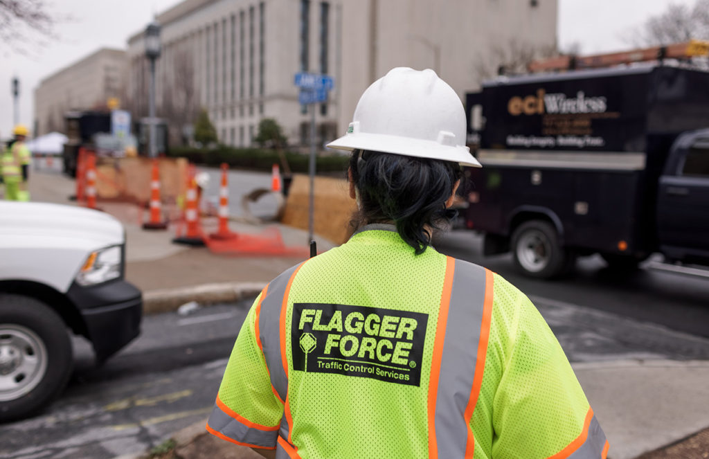 Back of Flagger Force employee in PPE on job site with eciWireless truck